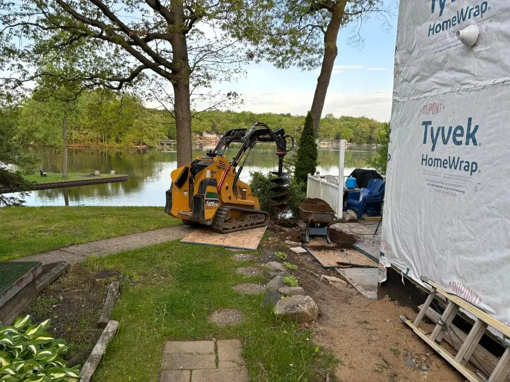 Vermeer compact track loader with auger drilling postholes at a lakeside home construction site