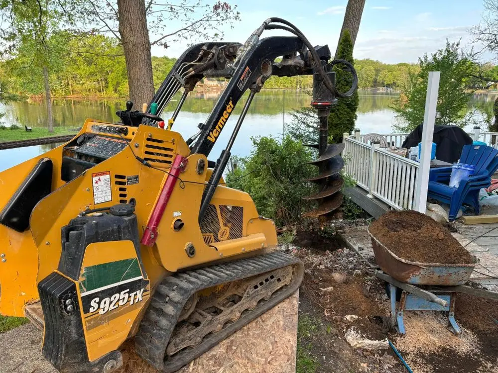 Close-up of Vermeer S925TX hydraulic auger with dirt-covered bit after drilling postholes