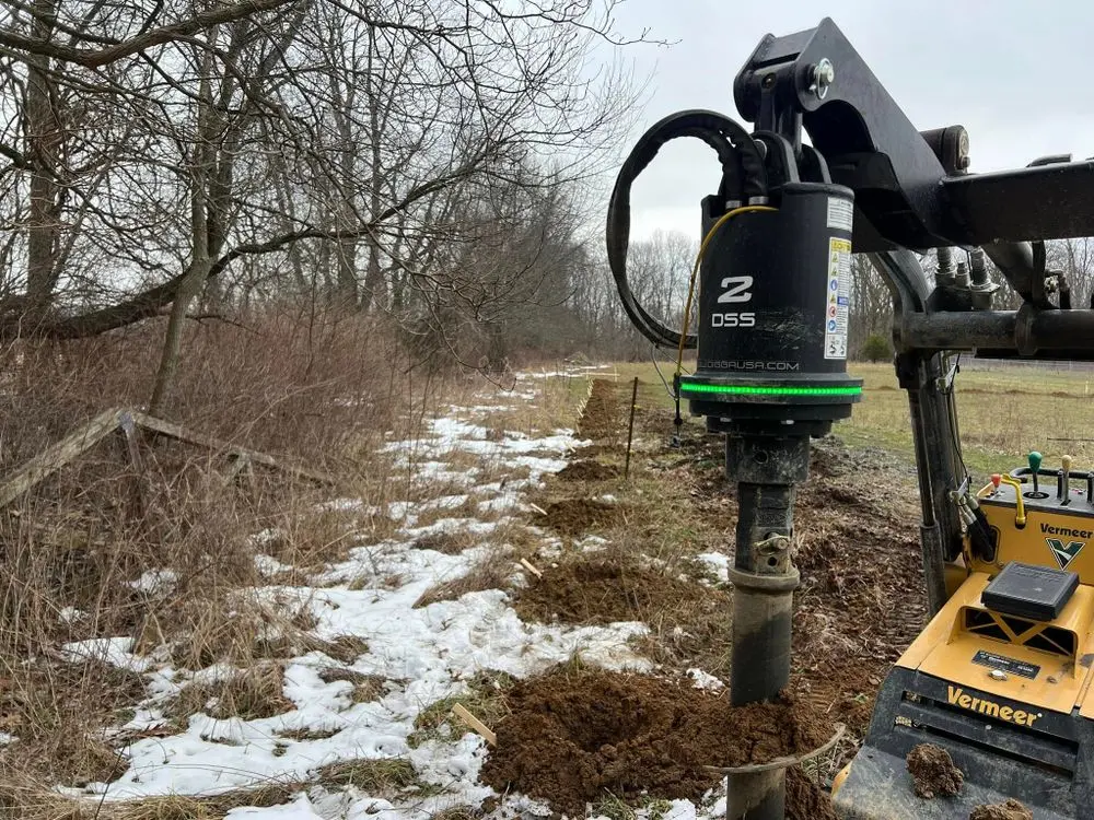 Close-up of auger bit drilling fence postholes in snowy ground during winter